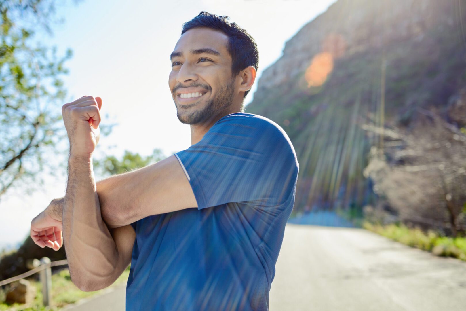 Smiling man outdoors stretching his arm on a sunny day.